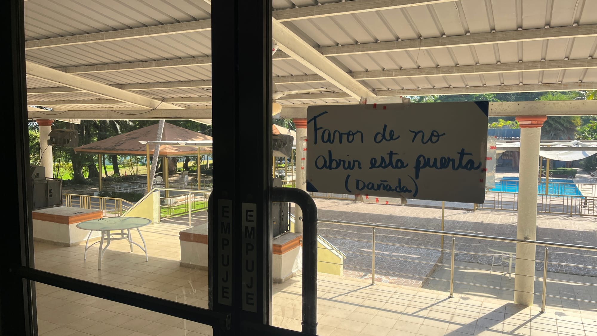 A glass door with a pasted paper reading "Favor de no abrir esta puerta (dañada)" (Please don't open this door [broken])