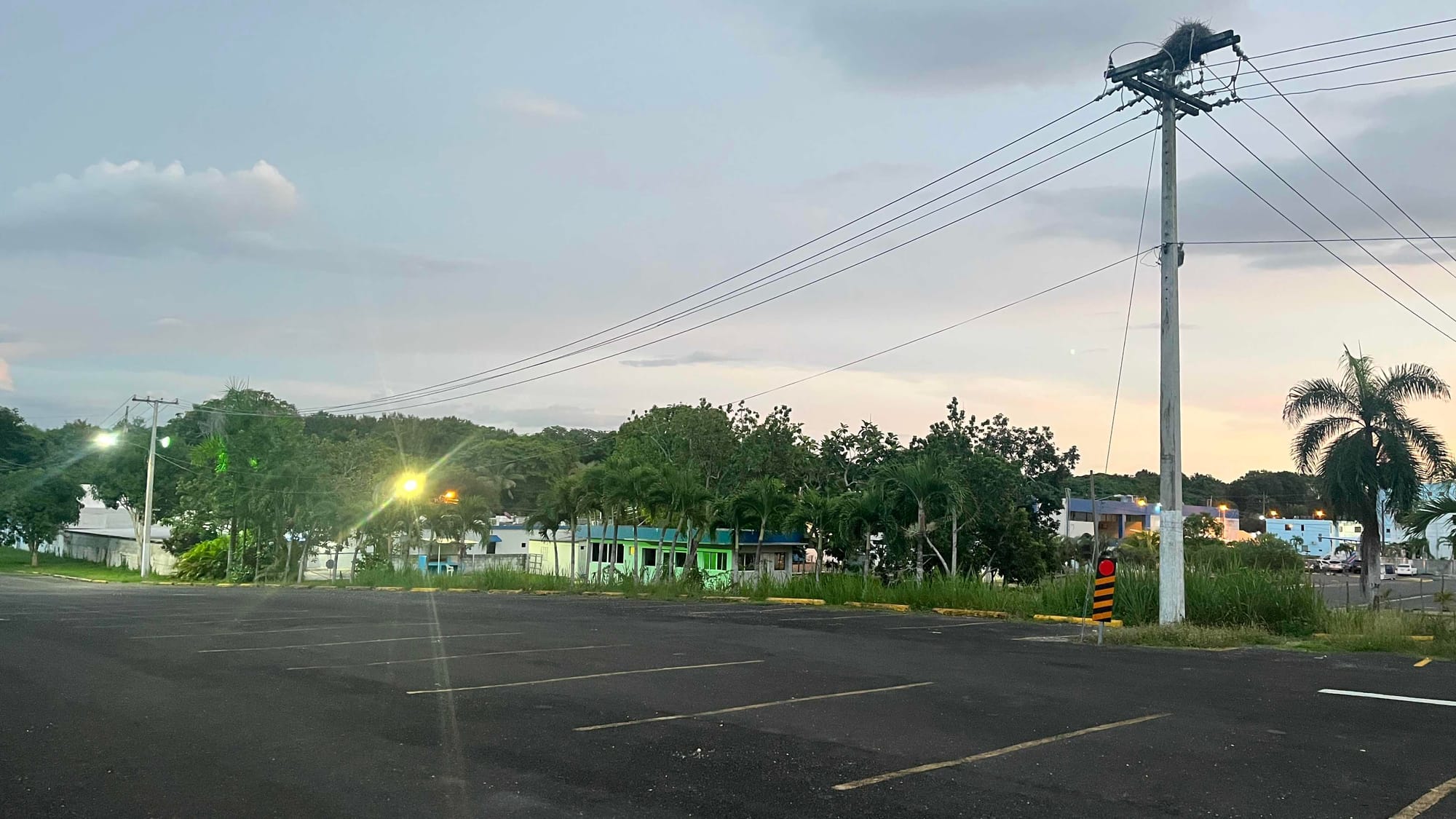 An image I took at the end of the competition outside the venue in the parking lot. The sky is at a gentle blue to orange sunset, trees in the background, an electricity pole in the foreground, and some small houses in the middle.