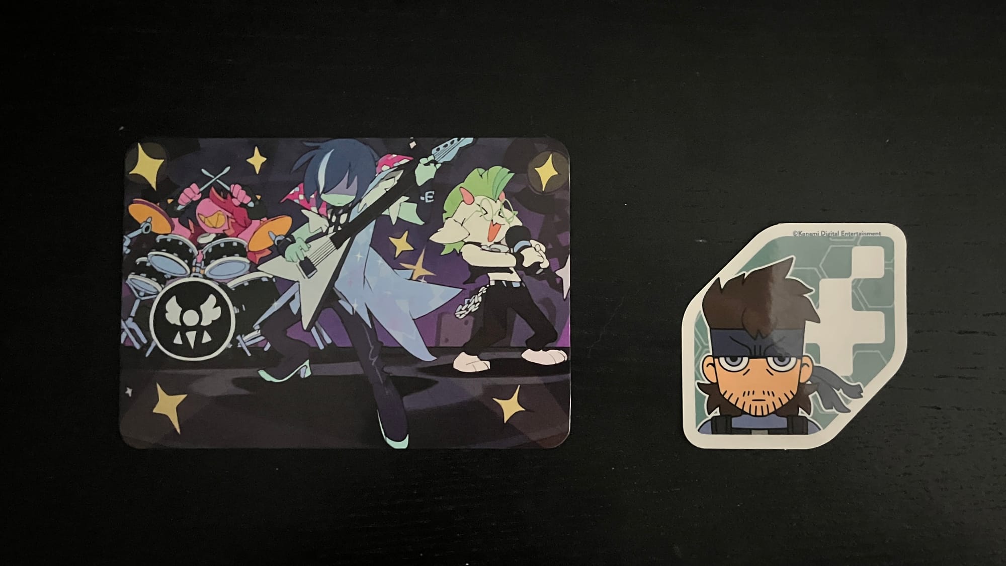 A Deltarune card featuring the Fun gang, and a Metal Gear Solid sticker featuring Snake, from Fangamer. 