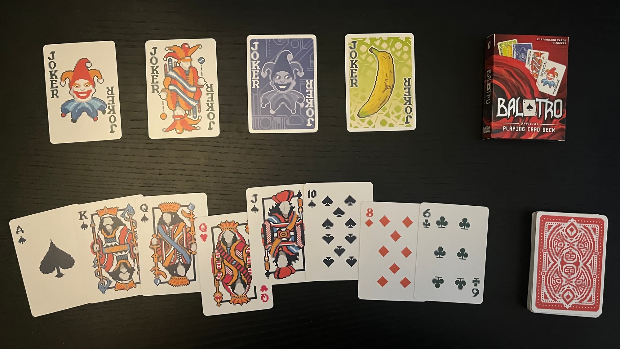 Some cards from the Balatro deck, all four jokers, the back of the deck, and the box they come in.