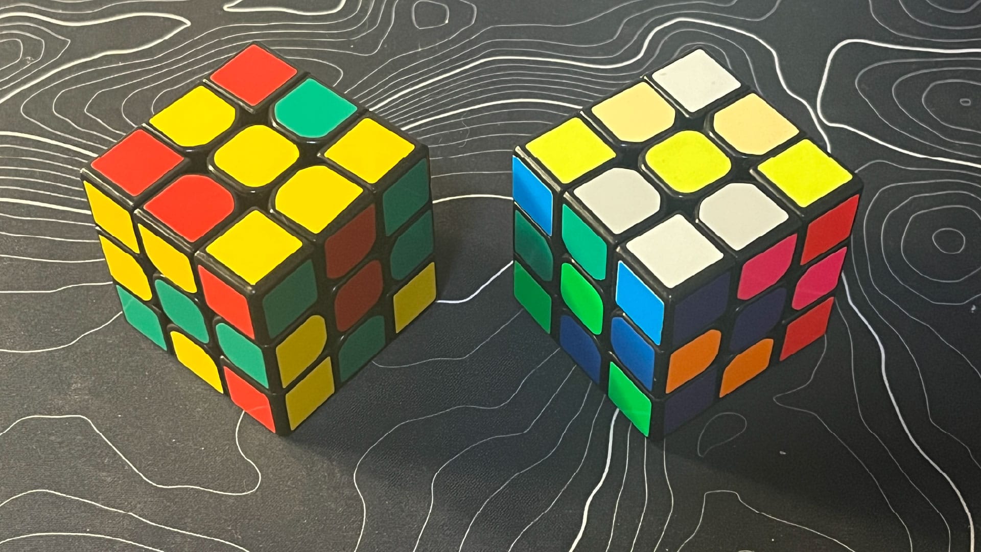 A 3x3 cube with just red, green, and yellow; and another 3x3 cube with red, orange, yellow, cream, green, fluorescent green, blue, fluorescent blue, white, light grey, purple, and pink.