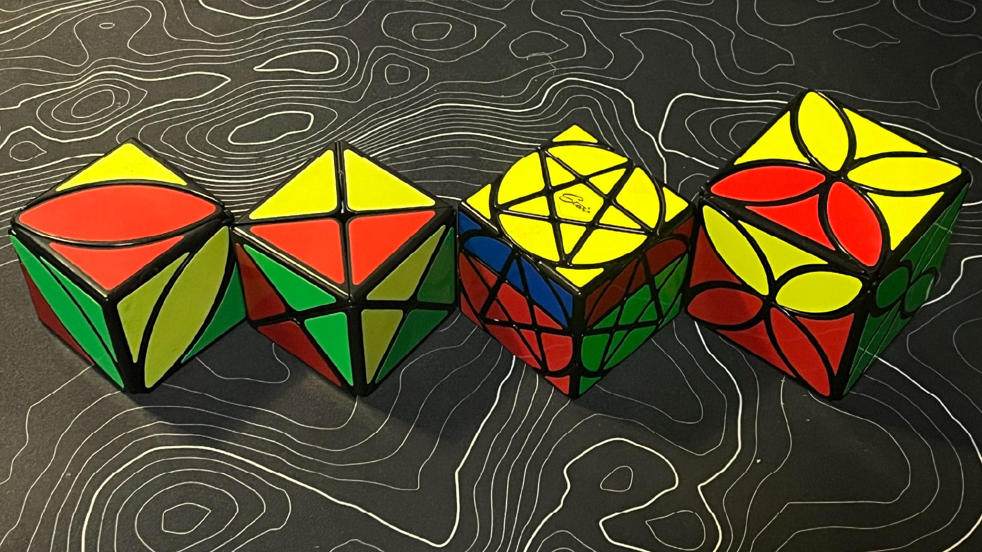 A QiYi Ivy Cube, ShengShou Dino Cube, QiYi Pentacle Cube, and QiYi Clover Cube, all with one turn made.