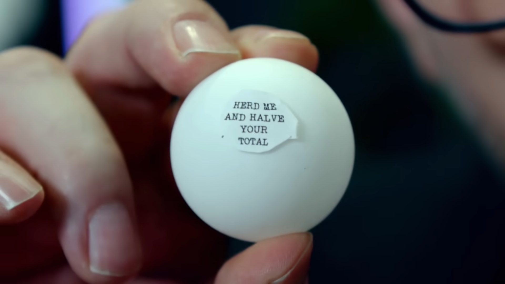Greg Davies holding a ping-pong ball that says "HERD ME AND HALVE YOUR TOTAL".