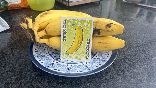 A Gros Michel card from the Balatro Playing Card Deck next to literal actual real-world bananas.